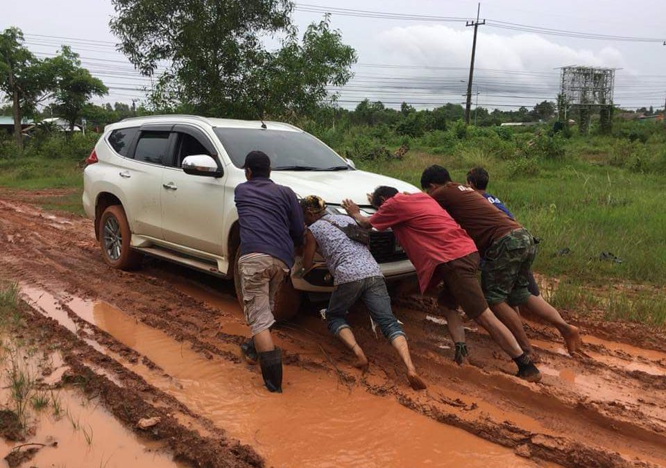 a group of young men pushing a car out of the mud