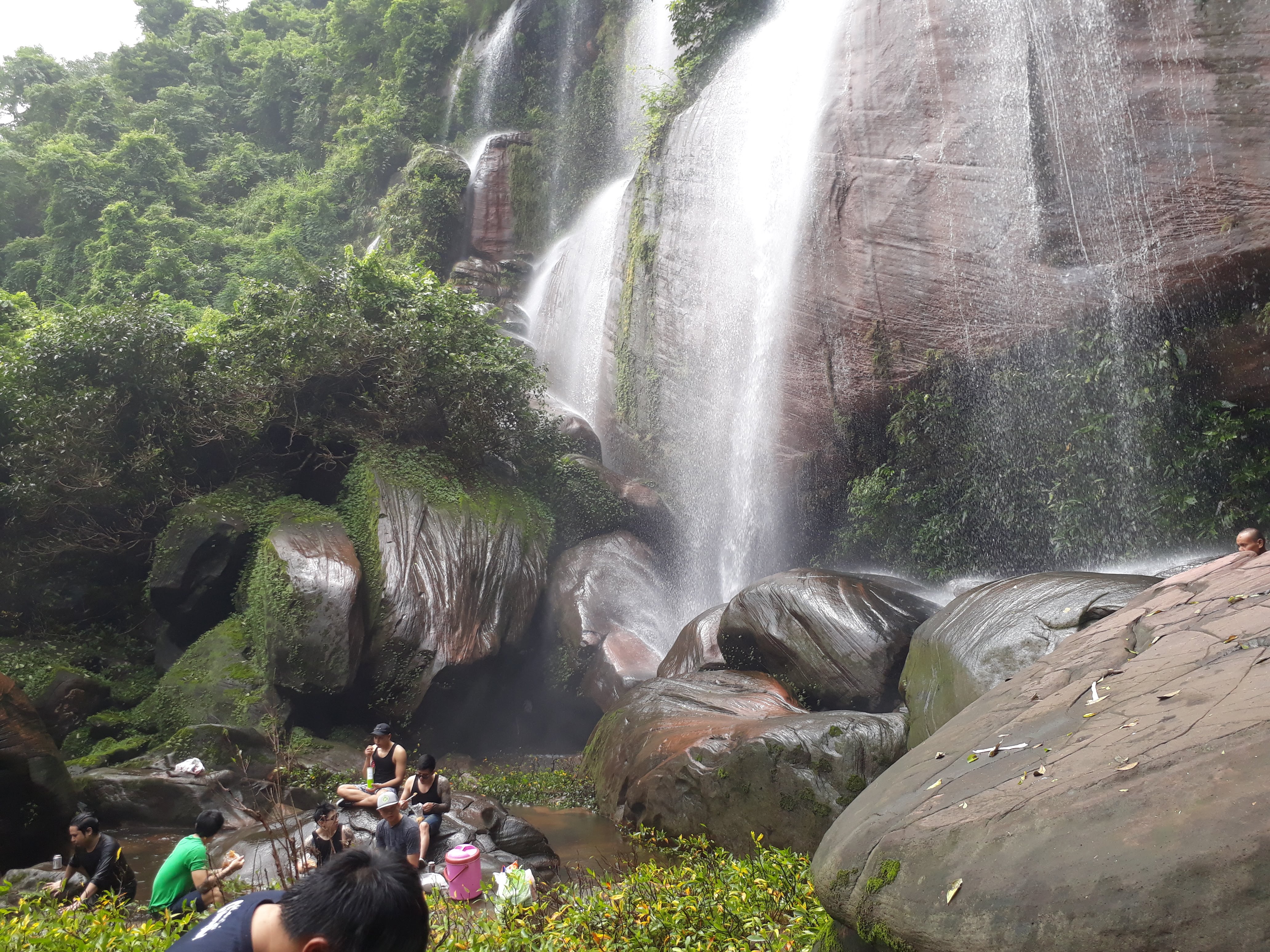 group of people sitting at the base of a waterfall eating lunch