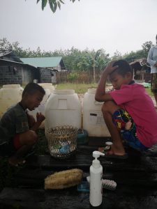 two young Thai boys crouch next to water buckets and brush their teeth