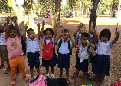 small kids stand in a line holding up new toothbrushes and toothpaste in a rural Thailand village