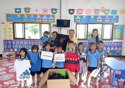 local partners lokgatat giving clothes to school kids, all pose with shirts and thank you sign for a photo