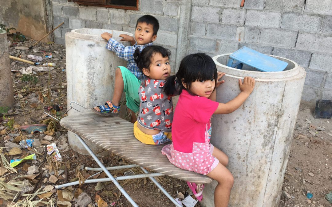 three kids in Thailand sit on an old iron board and look at the camera