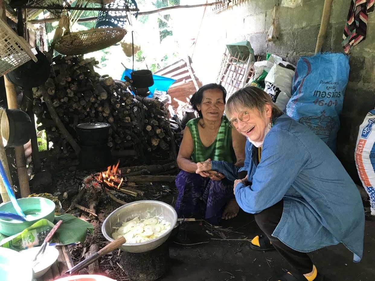 Thai elder Sompan sits on the ground next to an American woman