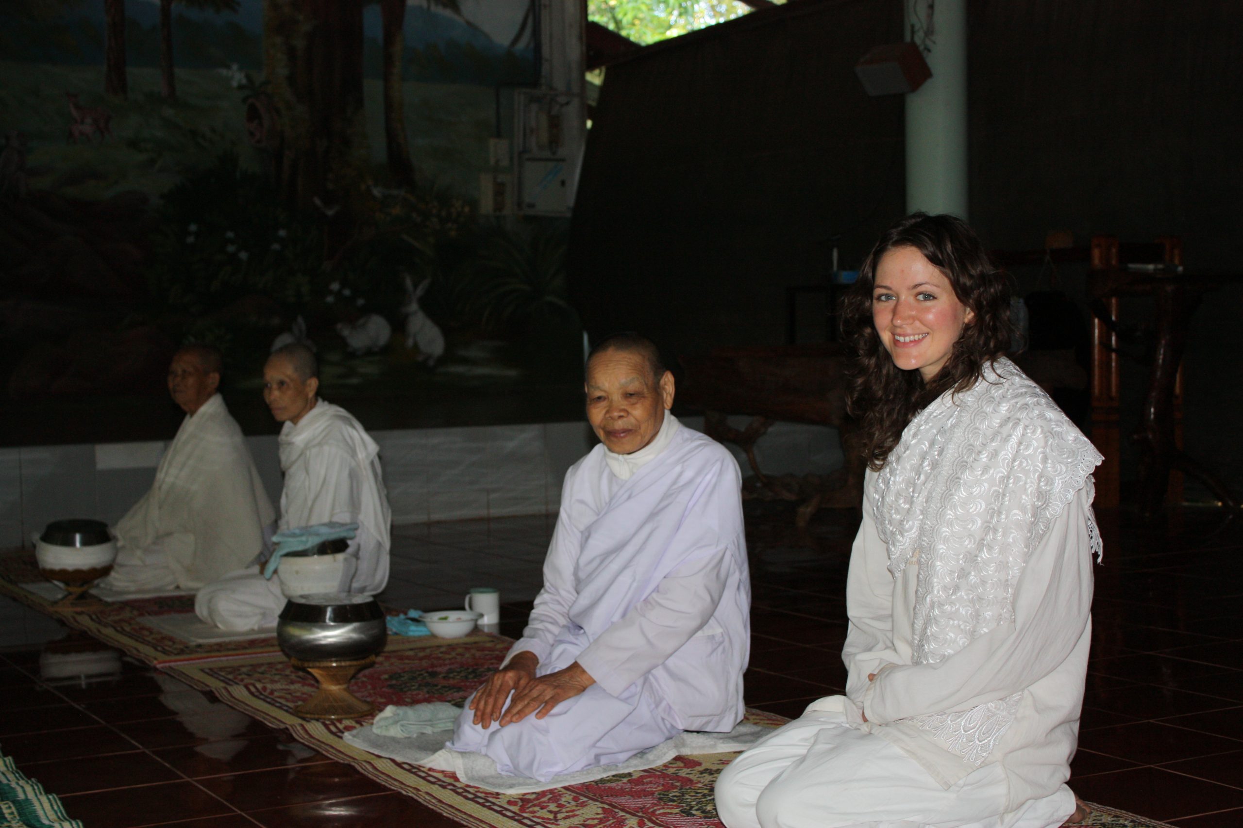 young woman sits in white robes with nuns in Thailand