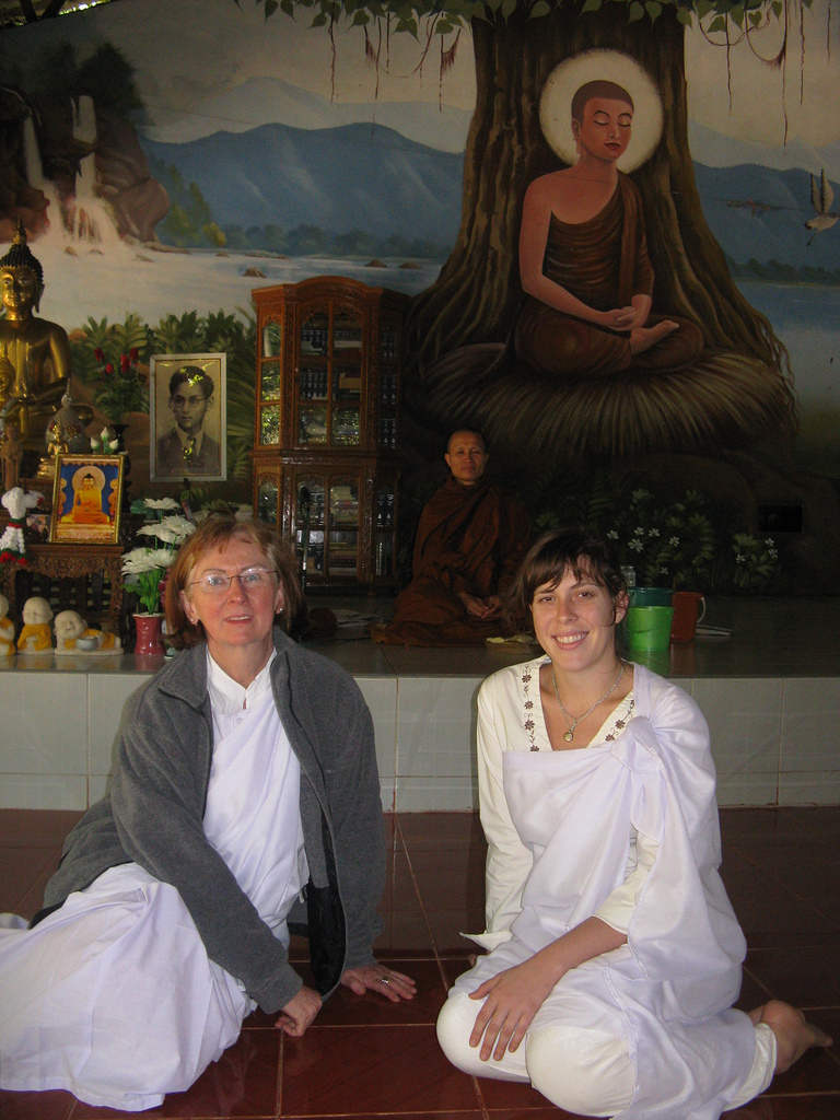 two women sit in a temple with a monk behind them